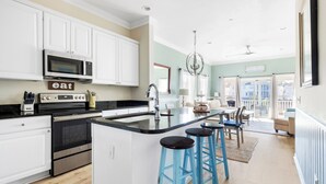 Una cocina moderna con armarios blancos, una isla central con taburetes azules y vistas al balcón.