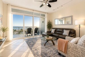 A living room with a sofa, a coffee table, a balcony with chairs, and a ceiling fan.