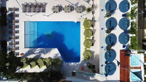 Vista aérea de un área de piscina de hotel con múltiples sillones y mesas, una gran piscina y varios jacuzzis.
