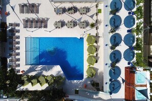 Vista aérea de un área de piscina de hotel con múltiples sillones y mesas, una gran piscina y varios jacuzzis.