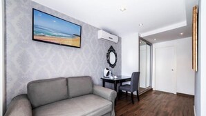 Una habitación moderna con un sofá gris, una pequeña mesa con una silla, un cuadro en la pared y un equipo de aire acondicionado.