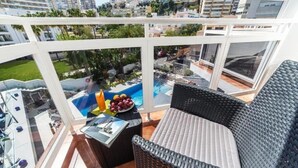 Un balcón con mobiliario de mimbre, piscina y vista a la ciudad.