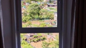 Una ventana con vista a una zona residencial, una mesita con una vela y cortinas.