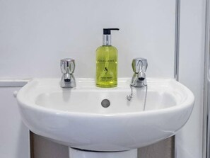 Un lavabo blanc pour la salle de bain, équipé d’un distributeur de savon liquide et de deux robinets.