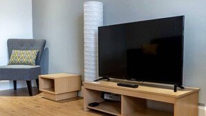 A modern living room with a wooden TV stand, a flat-screen TV, a grey armchair, and a small wooden side table. - ☆Bright Apartment, Near University + City Centre☆ (Dundee)
