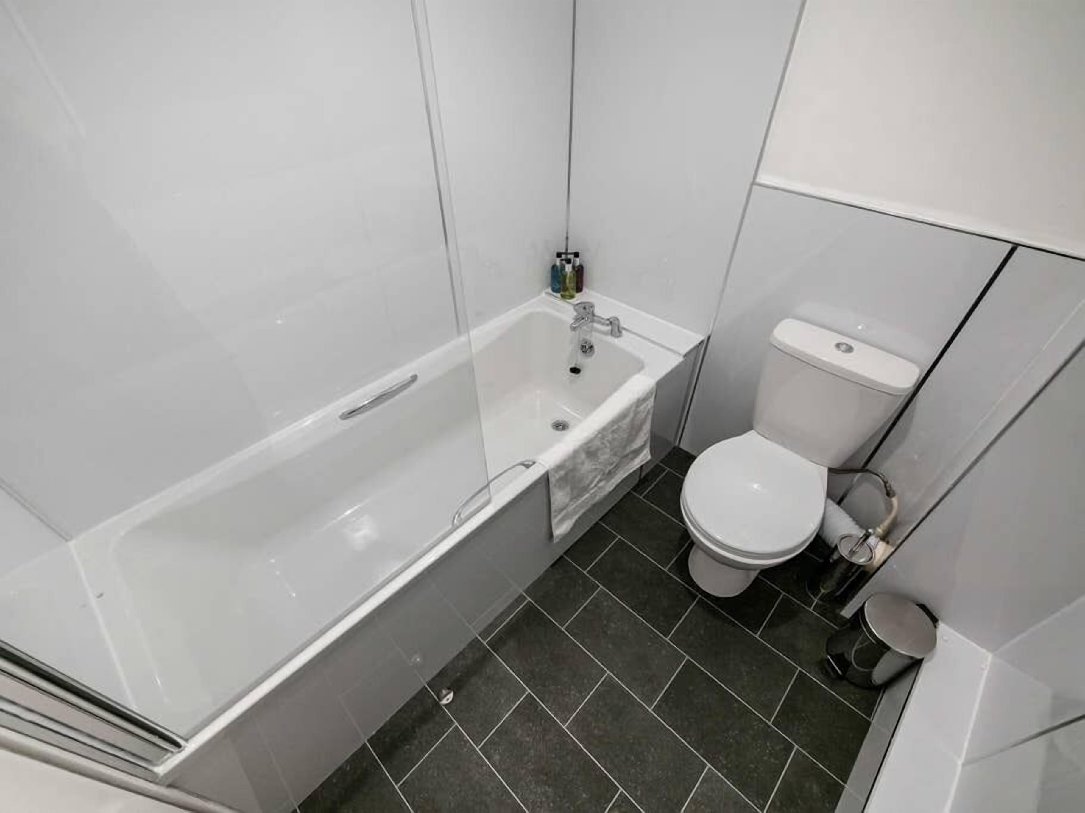 A bathroom with a bathtub, toilet, and dark tiled floor.