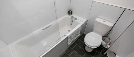 A bathroom with a bathtub, toilet, and dark tiled floor.