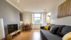 A modern living room with a grey sofa, wooden dining table, and a TV on a stand. - ☆Bright Apartment, Near University + City Centre☆ (Dundee)