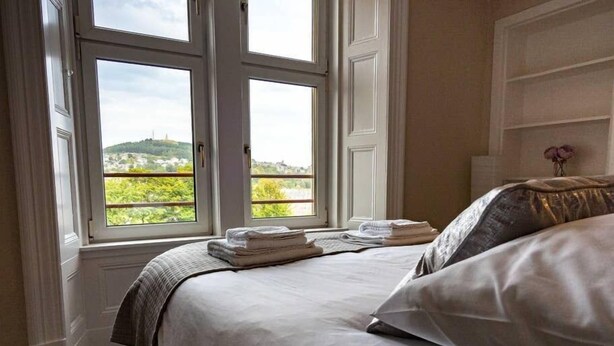 A bedroom with a bed, a window with a view of greenery, and a bedside table with folded towels. - ☆Bright Apartment, Near University + City Centre☆ (Dundee)