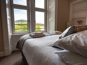 Ein Schlafzimmer mit Bett, Fenster mit Blick ins Grüne und Nachttisch mit gefalteten Handtüchern.