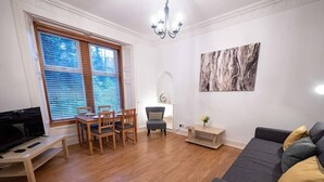 Un salon avec une table à manger en bois, des chaises, un canapé gris, un téléviseur et un tableau accroché au mur.