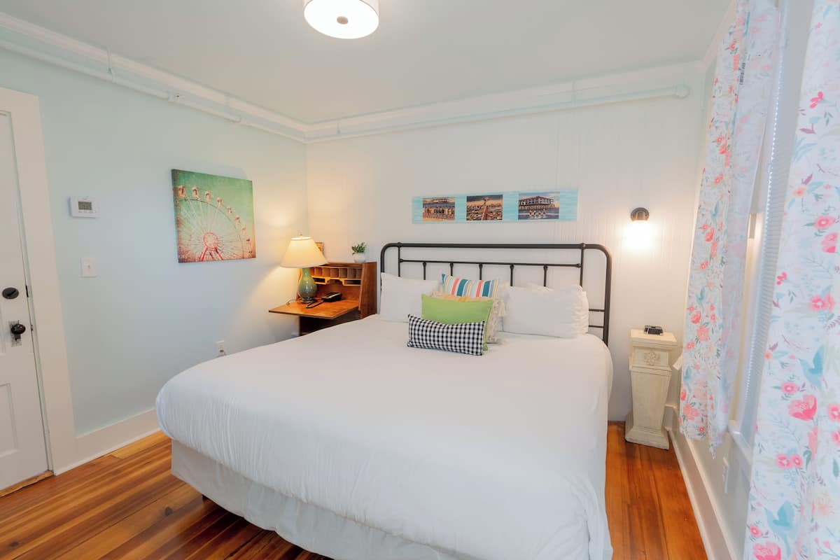 A bedroom with a large bed, a nightstand, a lamp, a wall clock, and a door.