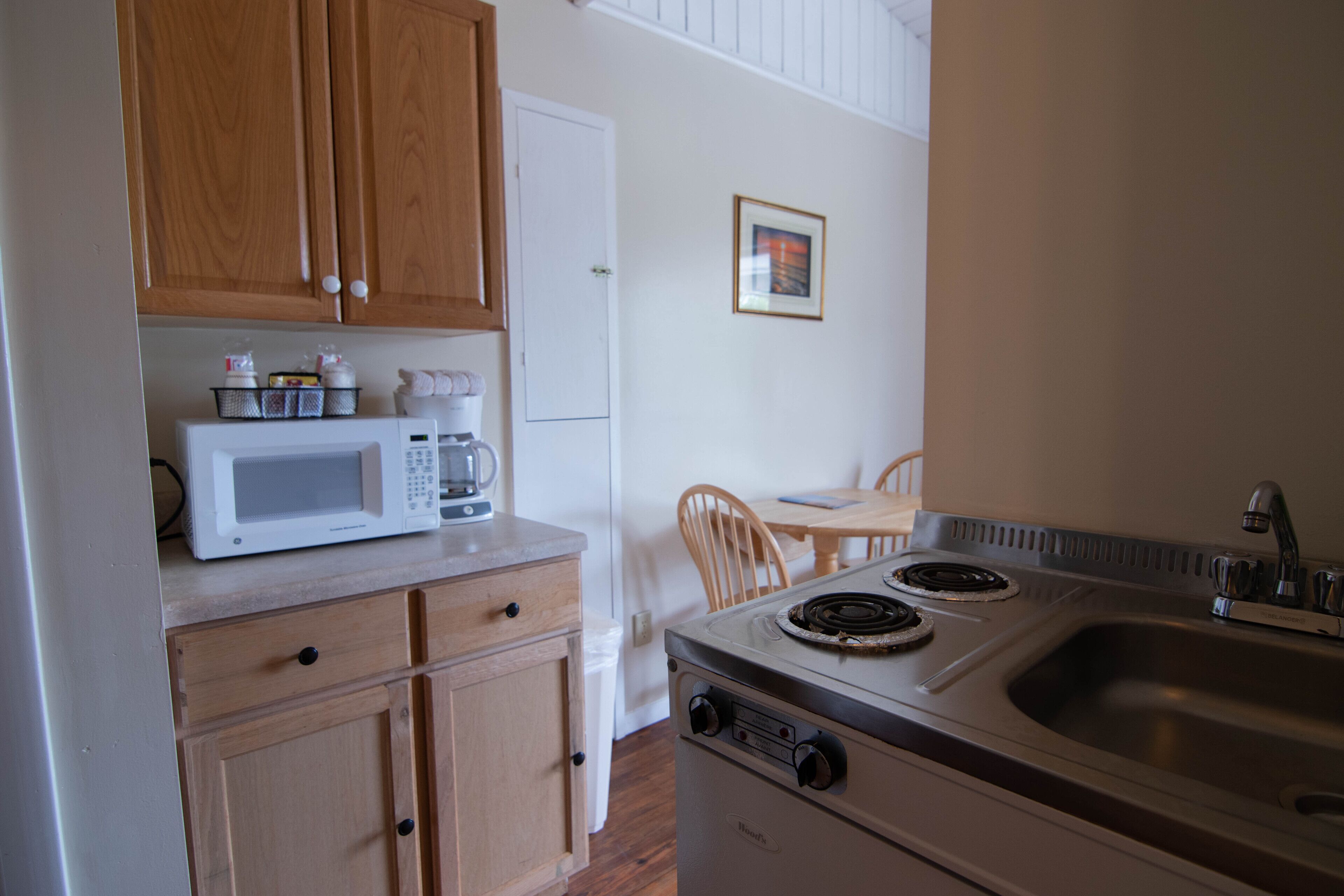 A compact kitchen with wooden cabinets, a microwave, a stove, and a sink.