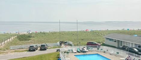 A pool area with a fenced deck, lounge chairs, and a view of the beach and ocean.
