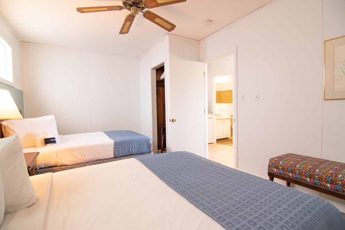 Ein Schlafzimmer mit Bett, einer Bank, einem Deckenventilator und einer offenen Tür zu einem Badezimmer.