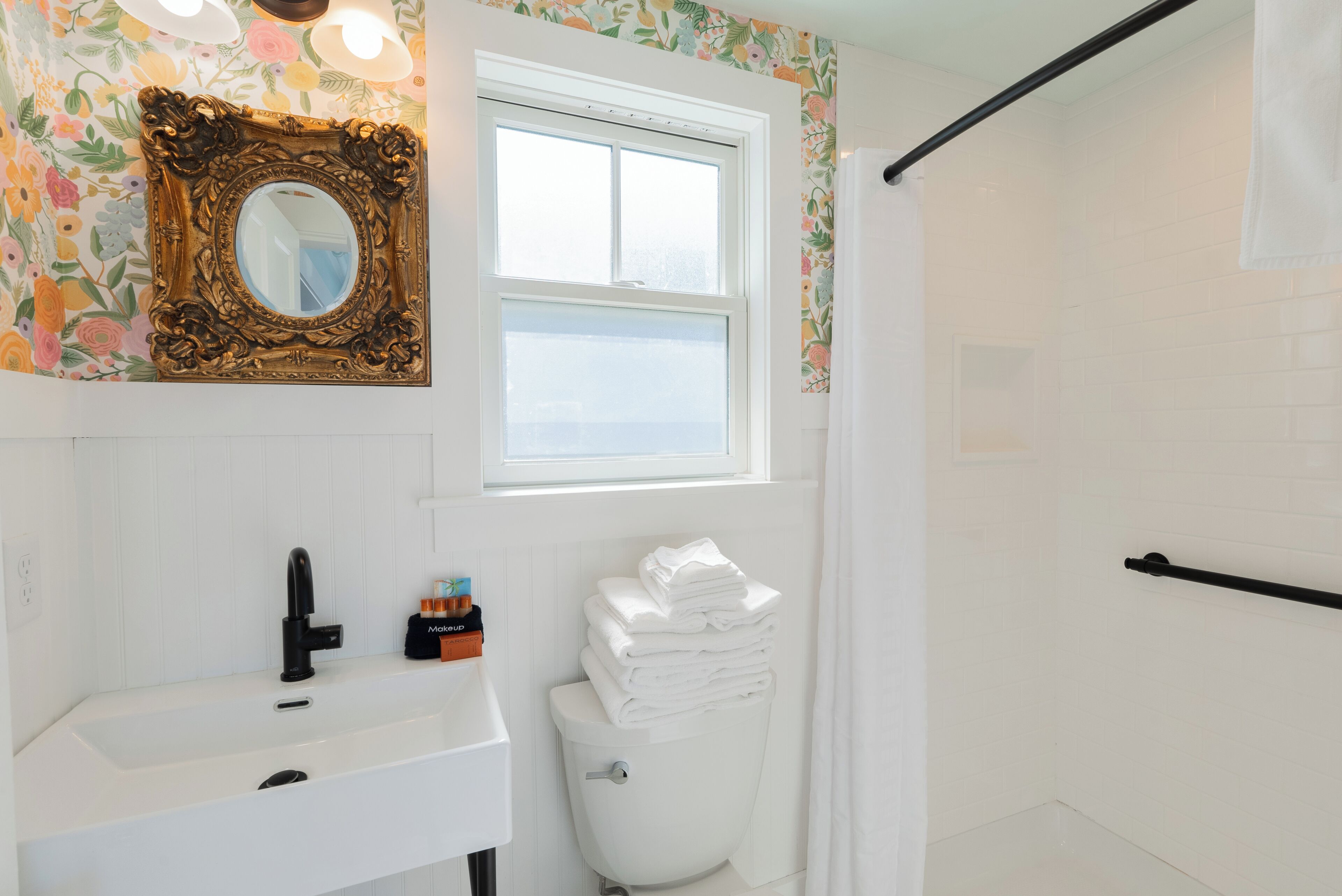 A bathroom with a white sink, a toilet, a mirror with an ornate frame, and a window.