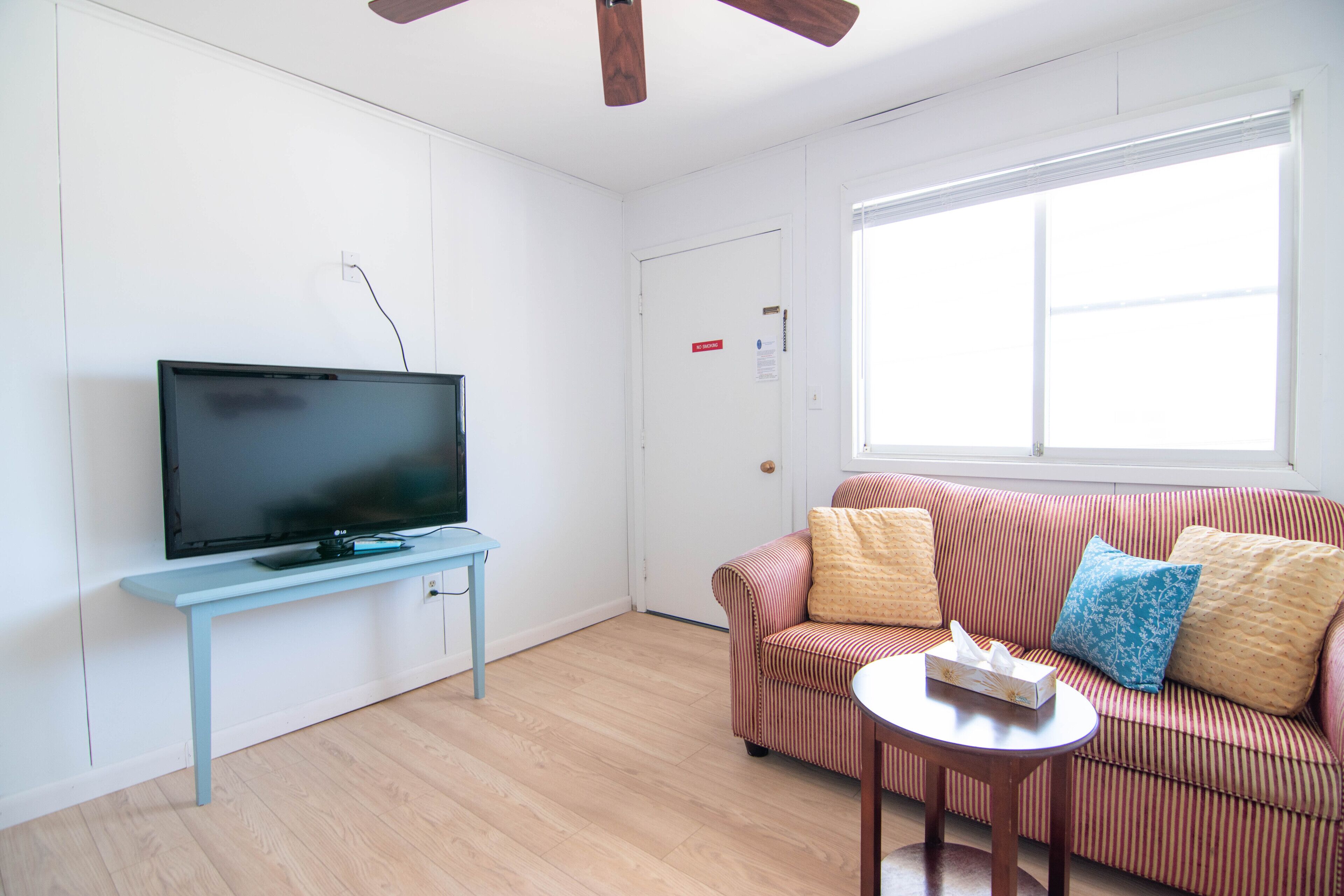 A living room with a flat-screen TV on a light blue stand, a striped sofa with cushions, and a small round table.