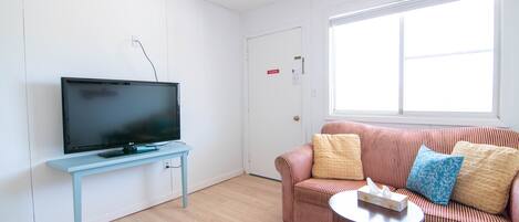 A living room with a flat-screen TV on a light blue stand, a striped sofa with cushions, and a small round table.