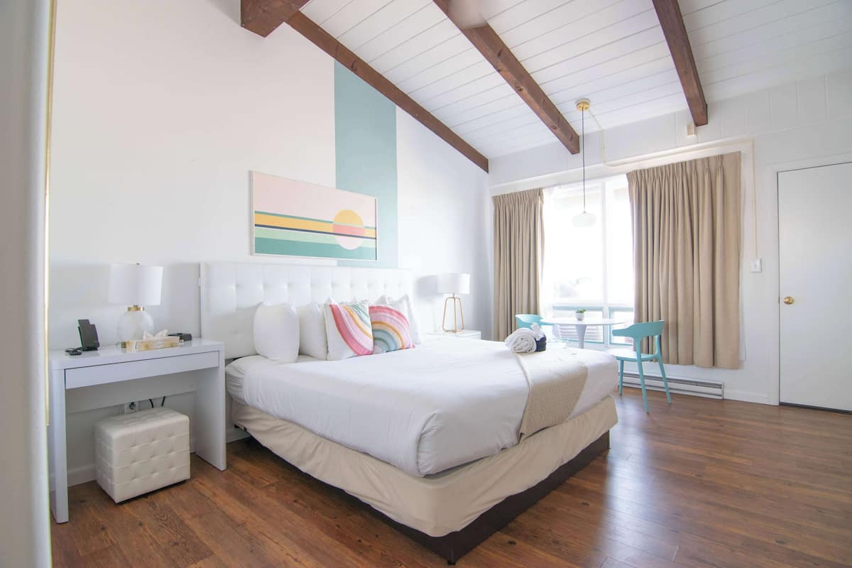 A bedroom with a bed, bedside table, chair, and a window with curtains.
