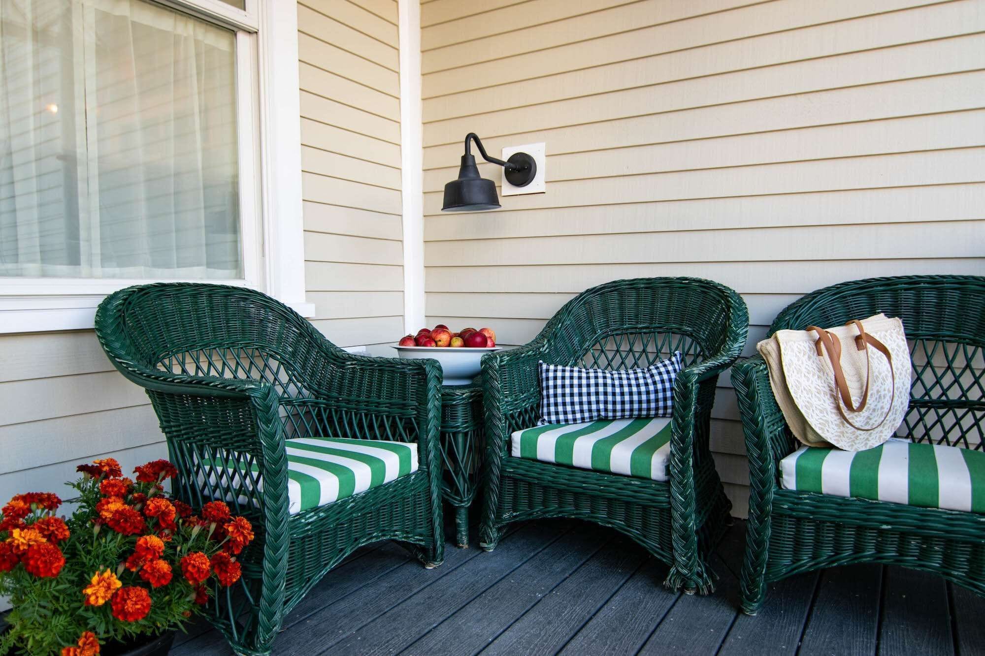 A porch with three wicker chairs, a small table with fruit, and a wall-mounted light fixture.