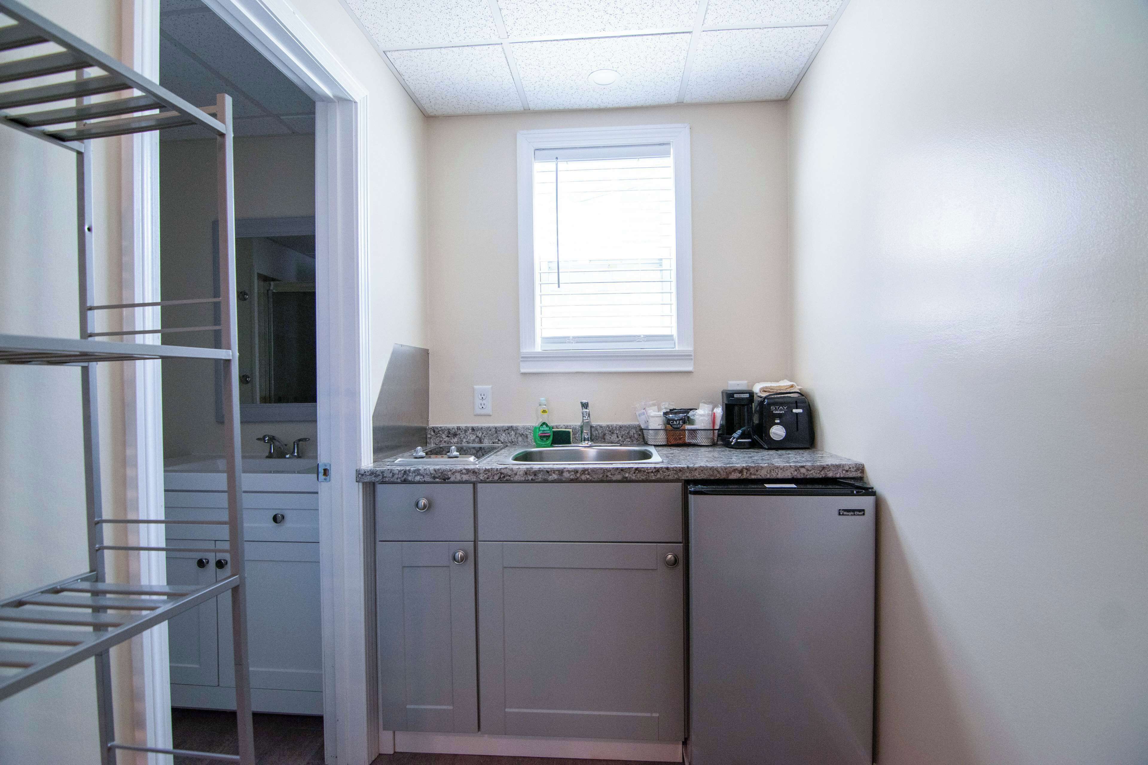 A compact kitchen with a built-in dishwasher, a window above the sink, and a metal shelf unit.