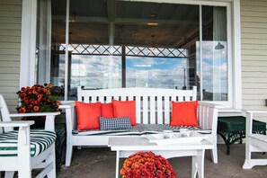 Eine weiße Veranda mit einer Bank, Stühlen und einem Tisch mit Krug und Tasse.
