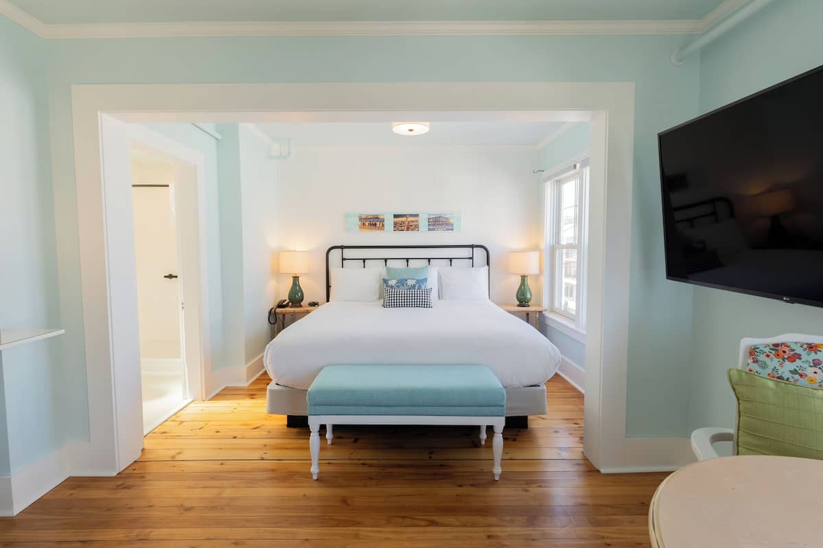 A bedroom with a bed, bedside lamps, a bench, and a TV.