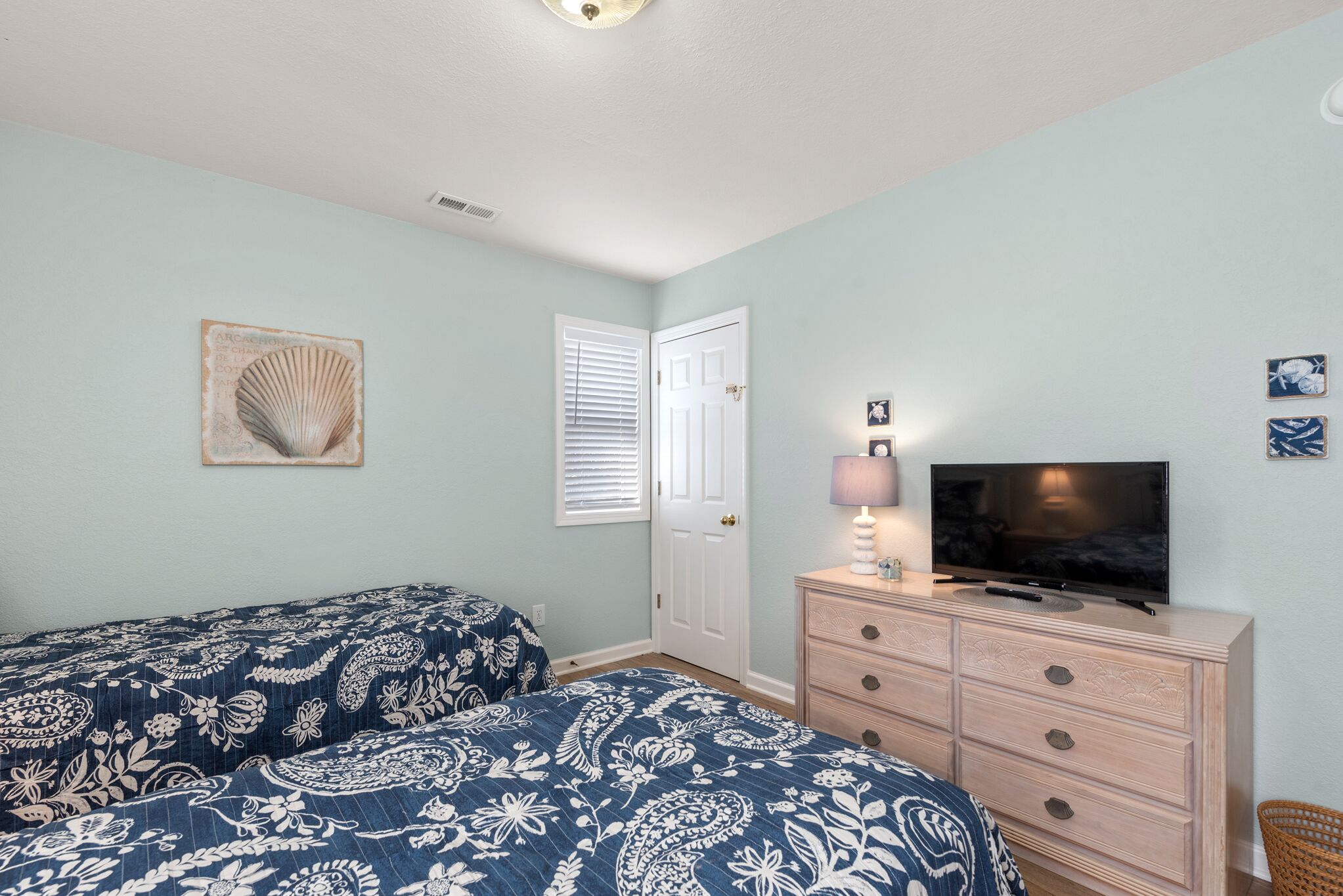 A bedroom with two beds, a dresser, a television, and a door with blinds.