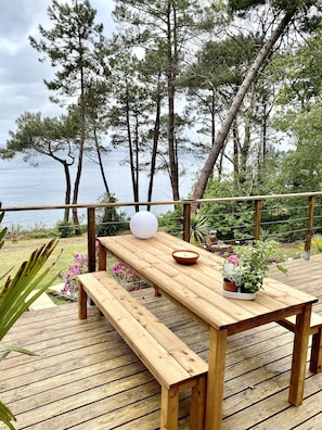 A wooden deck with a table and benches, overlooking a body of water with trees in the background.