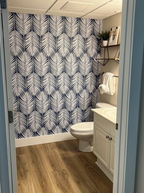 A bathroom with a patterned wallpaper, a toilet, a sink, and a wooden floor.