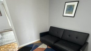 A living room with a black sofa, a colorful geometric rug, and a framed picture on the wall. - TwinCity 1 BR/1 BA- Minutes to NYC!  (Jersey City)