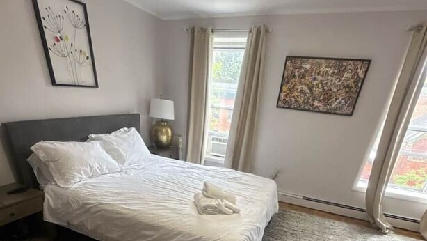 A bedroom with a bed, a nightstand, a lamp, and a window with curtains. - TwinCity 1 BR/1 BA- Minutes to NYC!  (Jersey City)