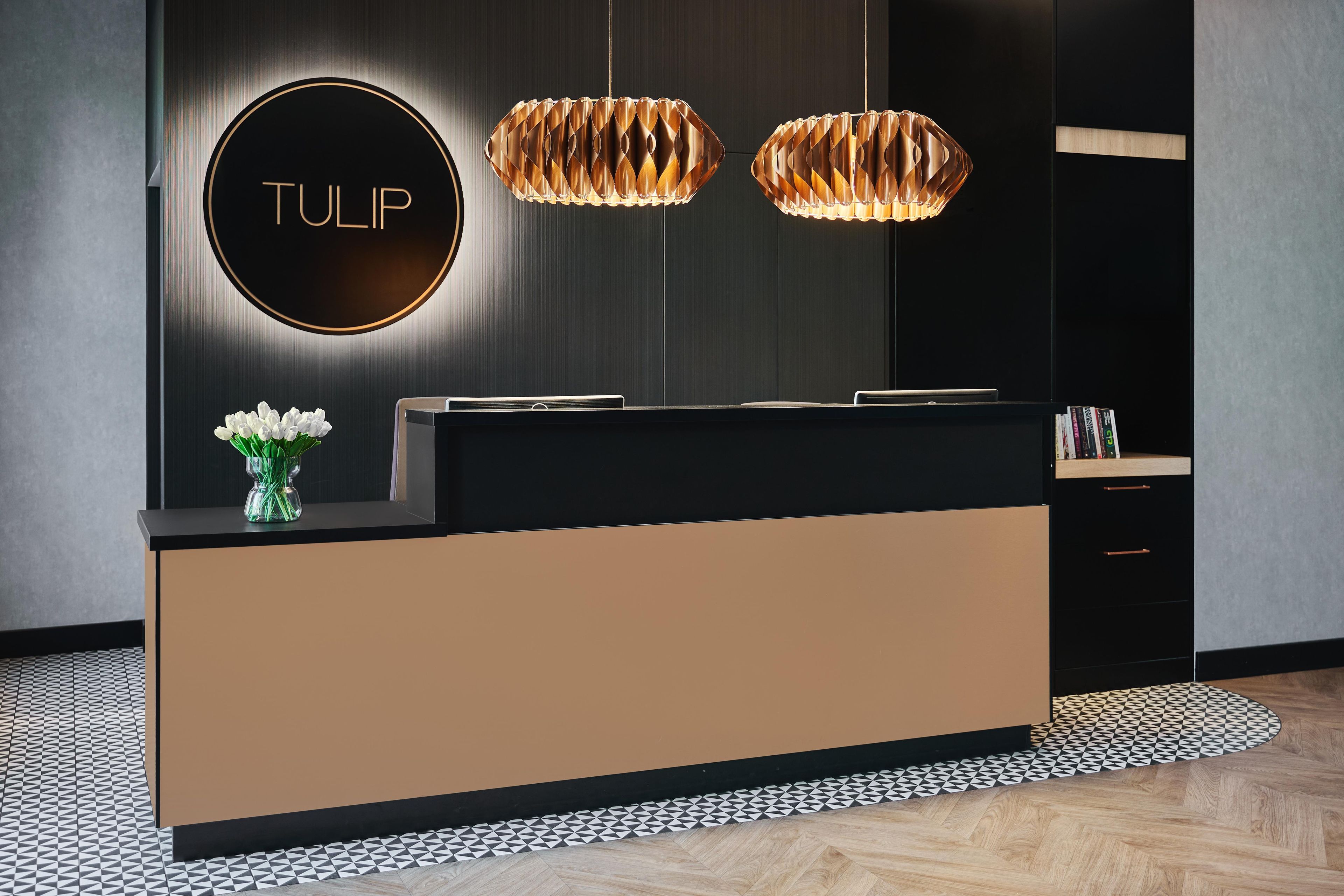 Un comptoir d’accueil au design moderne, un panneau circulaire portant le mot « TULIPE », et deux lampes suspendues.
