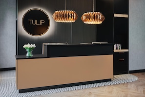 A reception desk with a modern design, a circular sign with the word 'TULIP', and two pendant lights. - Tulip Hotels & Residences Warsaw Targowa (Warsaw)
