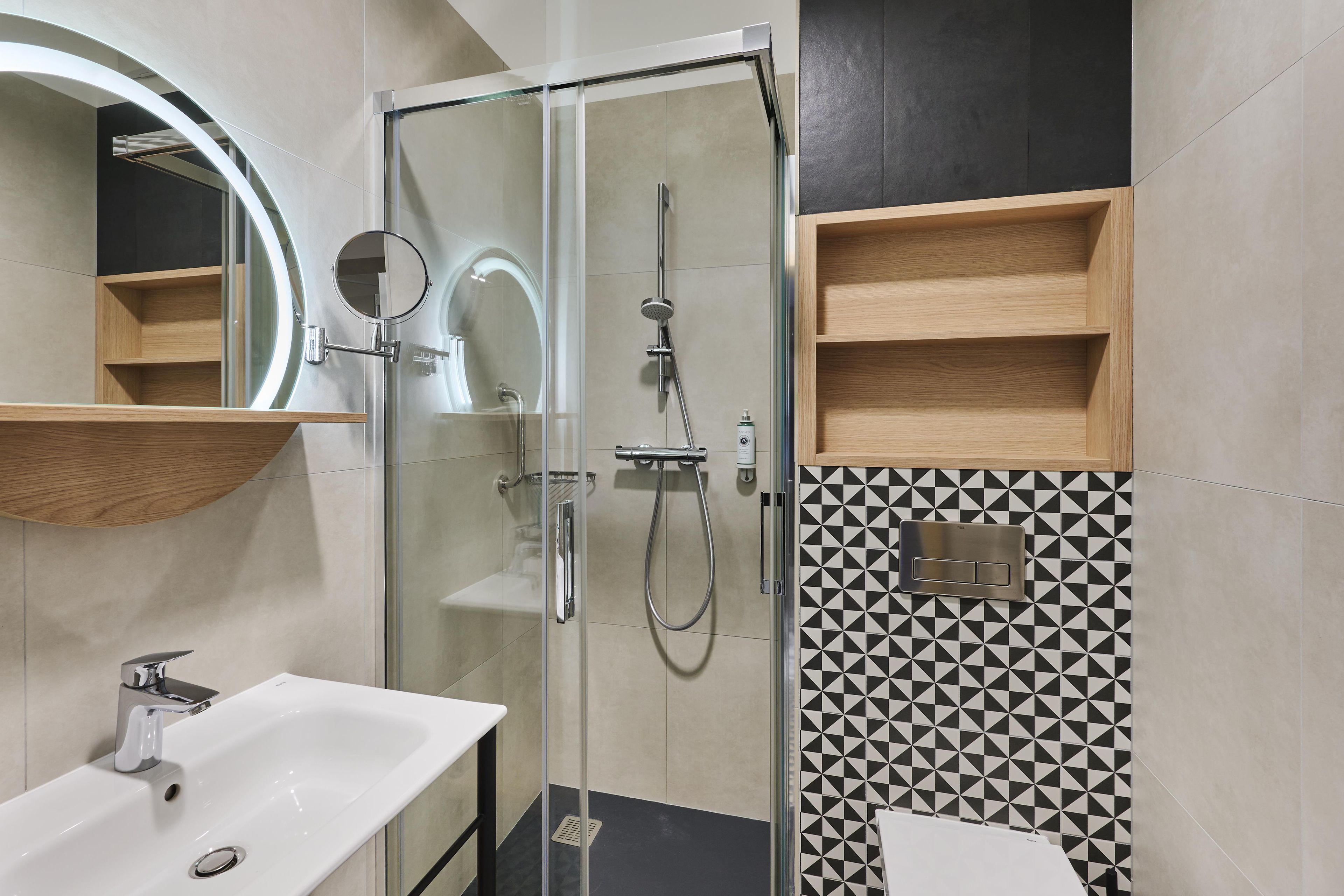 Un baño moderno con ducha envuelta en cristal, un lavabo blanco y un espejo con marco circular.