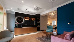 Een moderne hotellobby met een receptiebalie, een zithoek en een blauwe accentmuur.