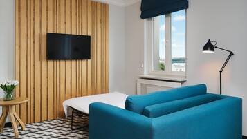 Una habitación con una cama, un televisor fijado a una pared de madera, una ventana con vistas, una lámpara y una mesita con un jarrón.