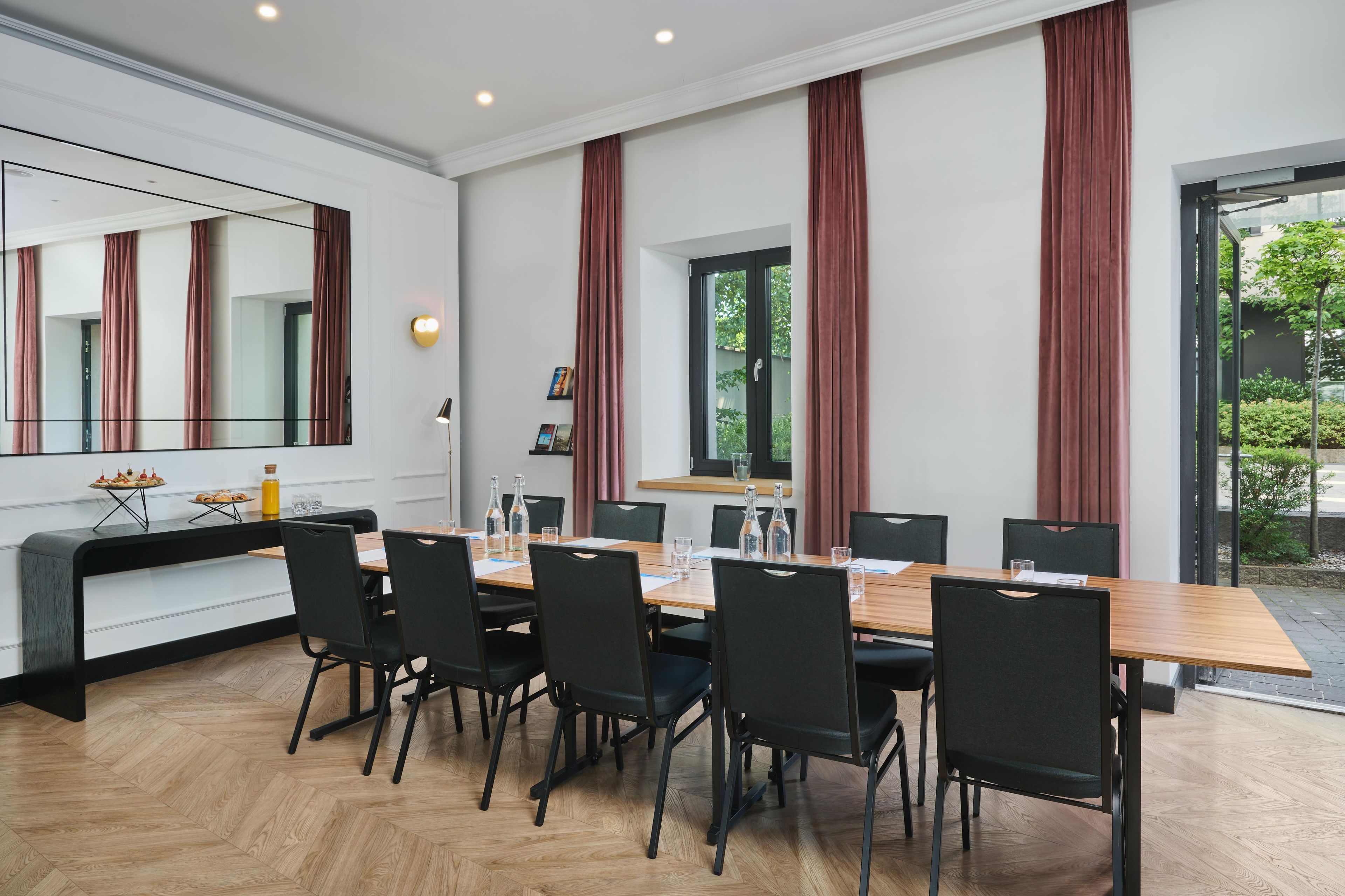 A modern dining area with a long table, black chairs, and a large mirror above.