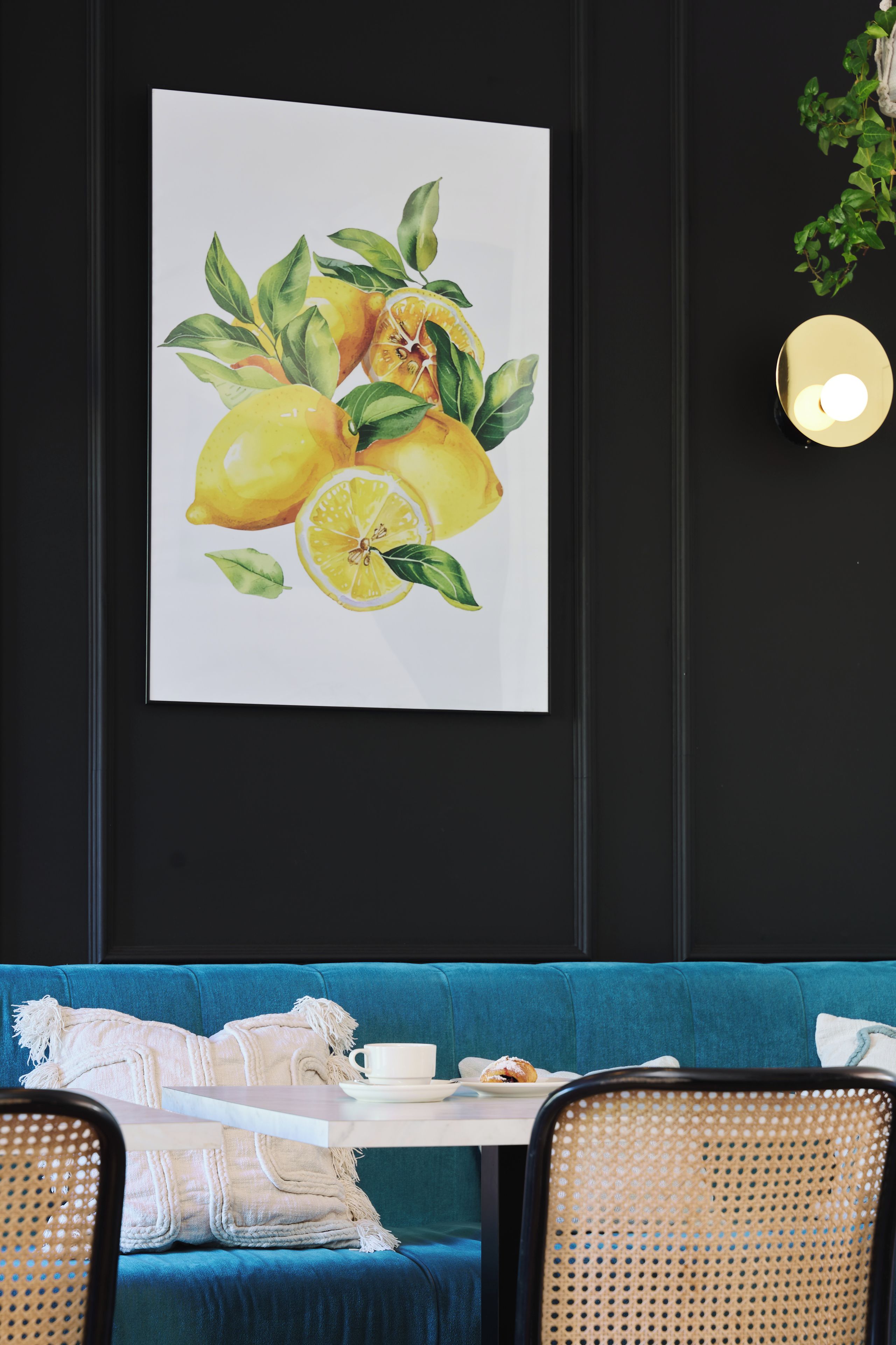Quarto com sofá azul, mesa branca com xícara e prato, e parede com quadro de limões e folhas.