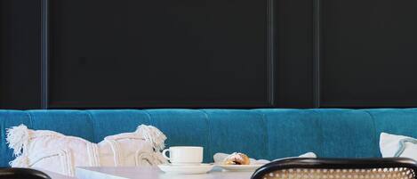 A room with a blue sofa, a white table with a cup and a plate, and a wall with a framed artwork of lemons and leaves.