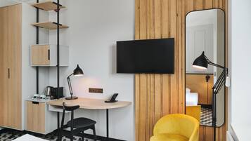 Habitación de hotel con escritorio, silla, televisor de pantalla plana, espejo y sillón amarillo.
