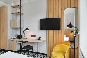 Habitación de hotel con escritorio, silla, televisor de pantalla plana, espejo y sillón amarillo.