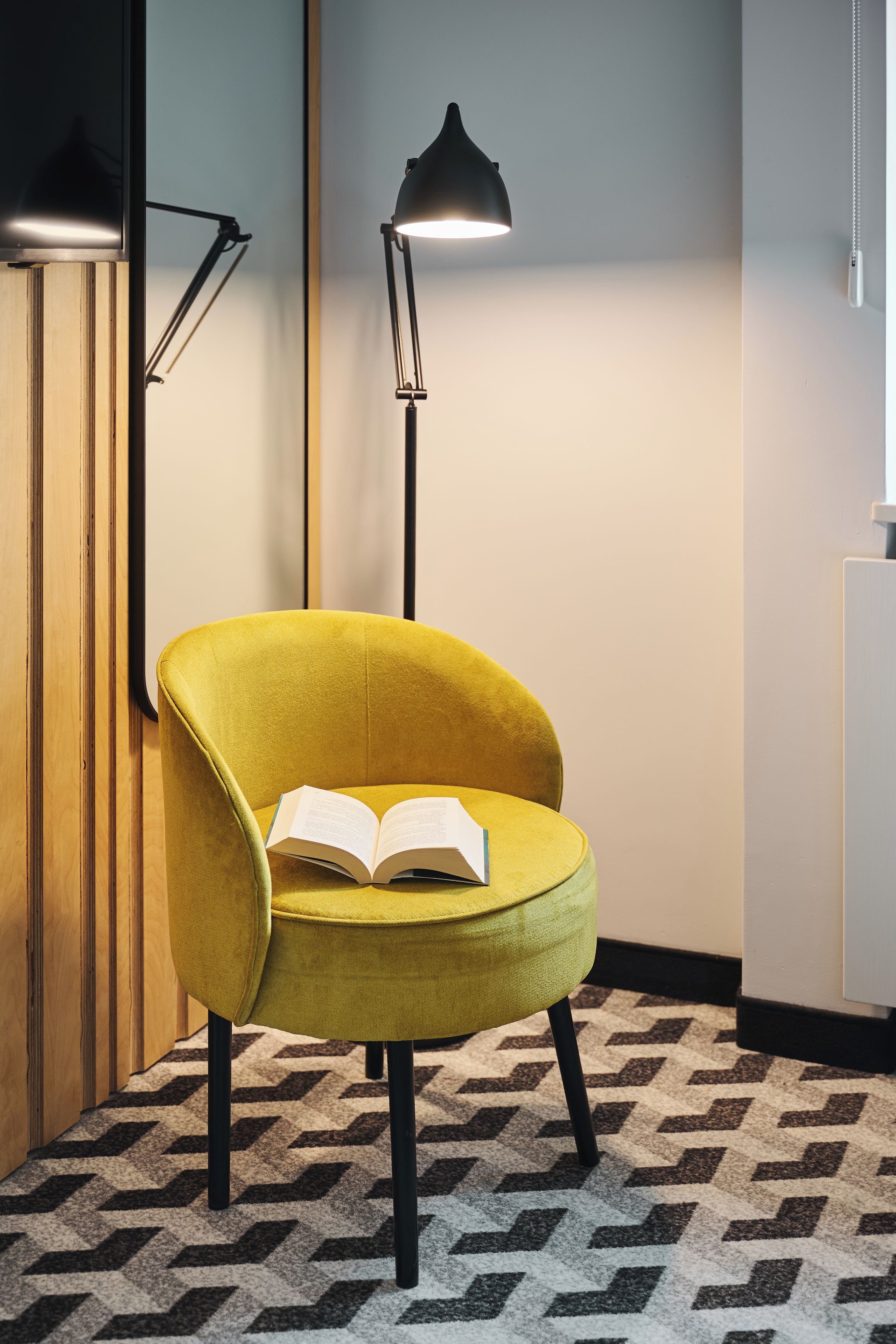 A yellow armchair with an open book, a floor lamp, and a patterned carpet.