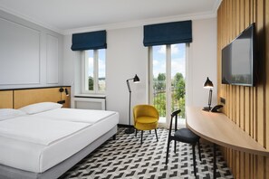 Une chambre d’hôtel équipée d’un lit, d’un bureau, d’une chaise, d’une télévision et offrant une vue sur l’extérieur.