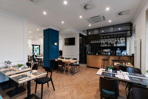 Un restaurant moderne avec un plancher en bois, une décoration en noir et blanc et un bar doté d’étagères remplies de verres et de bouteilles.
