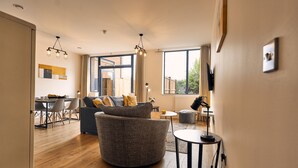 Una sala de estar moderna con un sofá redondo gris, un comedor con mesa y sillas, y ventanas amplias que ofrecen vistas al exterior.