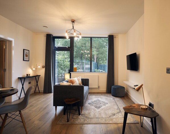 Una sala moderna con un sofá, una mesa de centro, un televisor montado en la pared y un ventanal con vistas a zonas verdes.