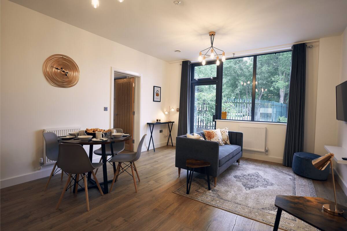 A modern living room with a sofa, chairs, a dining table, and a large window with a view of trees.