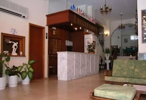 A reception area with a marble counter, potted plants, a green sofa, and a staircase. - Anamar Zante Hotel (Zakynthos)
