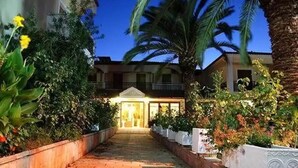 A pathway leading to a building with a central entrance, surrounded by greenery and palm trees.